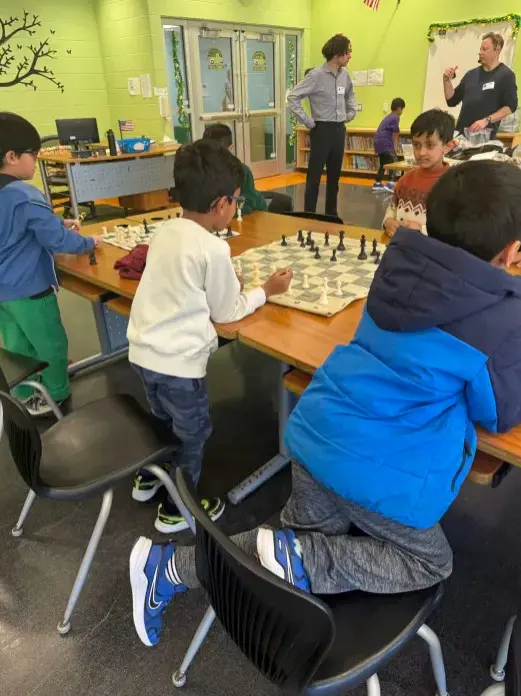 Students playing chess at tables in a library with a bright green wall.